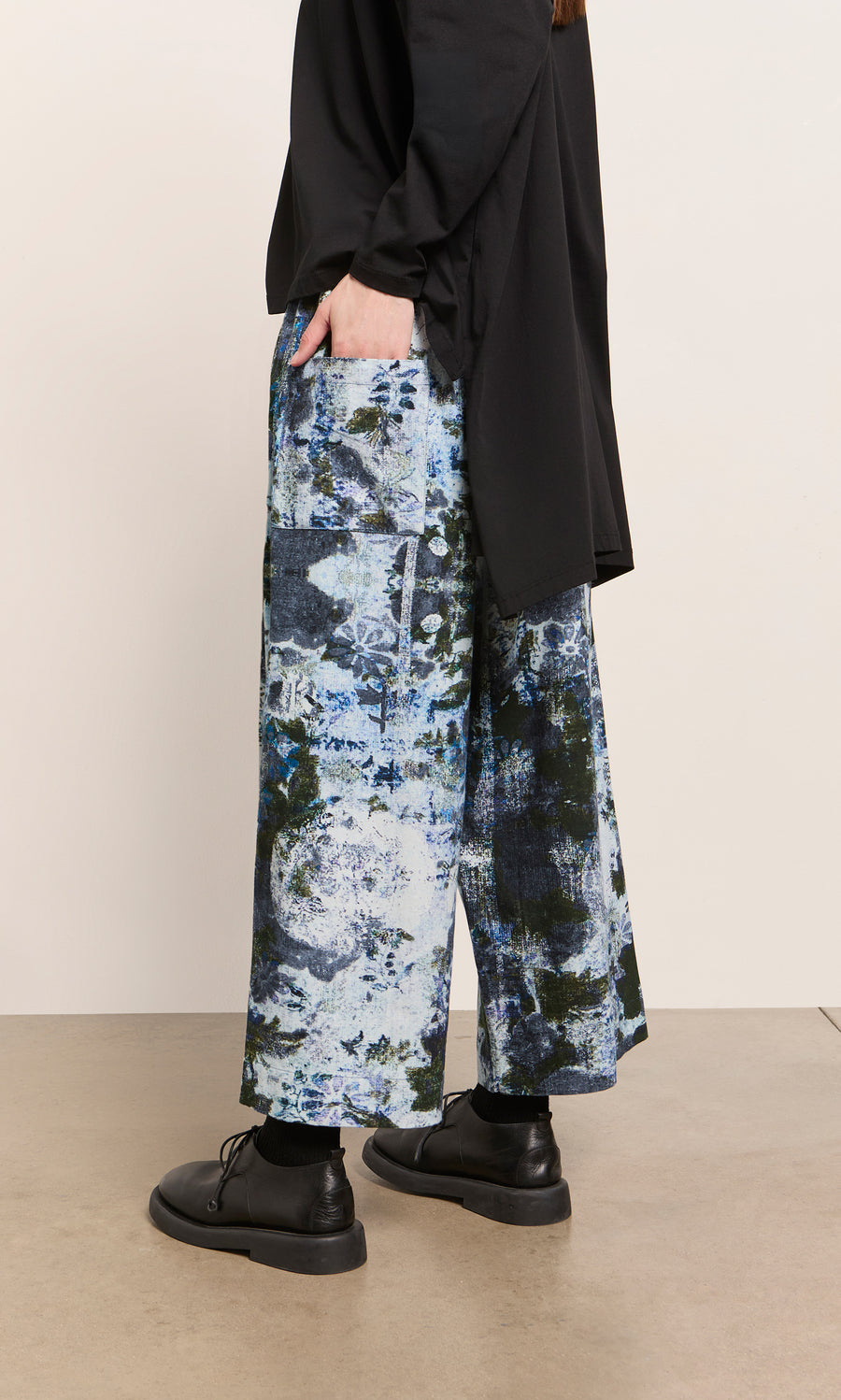 Plümo  Person in black top and shoes wears Caccia Pants with a wintery print, standing indoors.