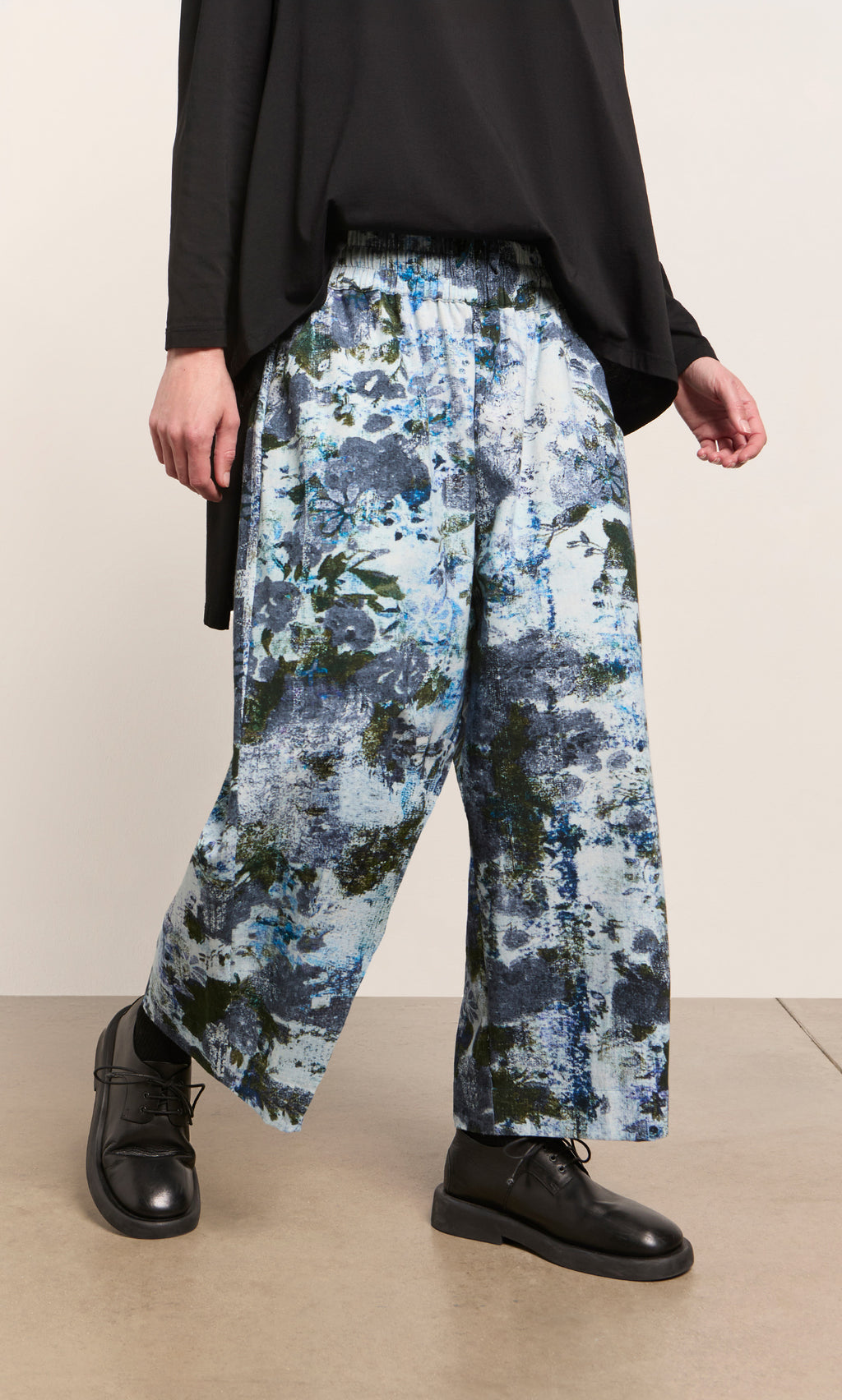 Plümo  Person wearing Caccia Pants with an impressionistic winter print, black top, and black shoes, standing indoors.