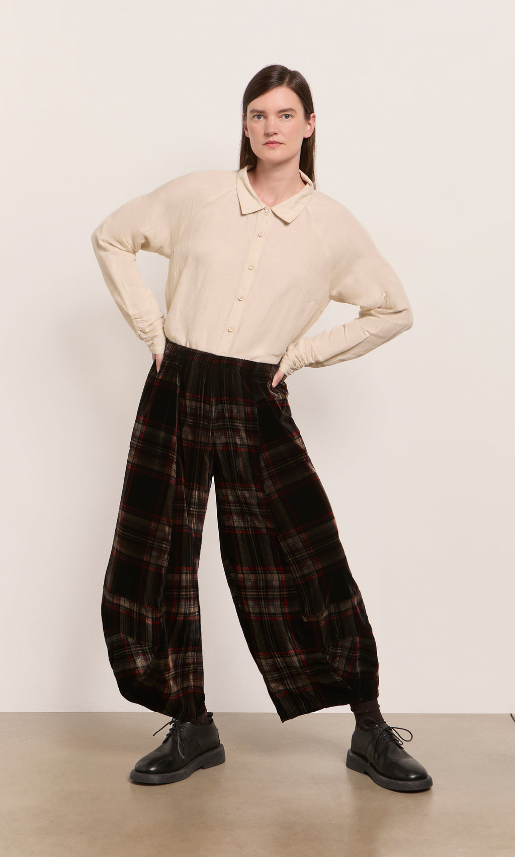 Plümo  Person stands hands on hips, wearing a beige shirt, Carson Tartan Pants in velveteen, and black shoes.
