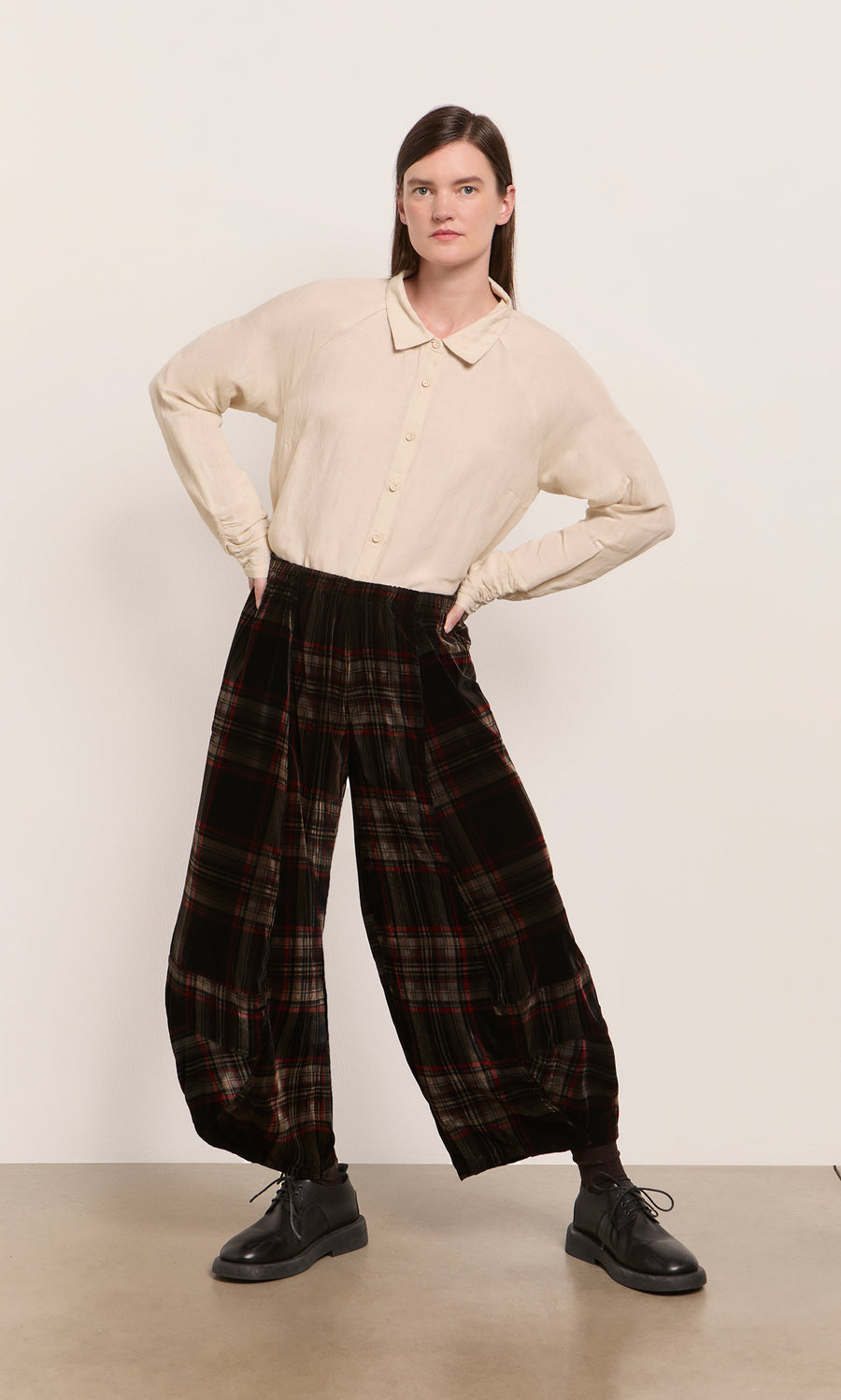 Plümo  Person stands hands on hips, wearing a beige shirt, Carson Tartan Pants in velveteen, and black shoes.
