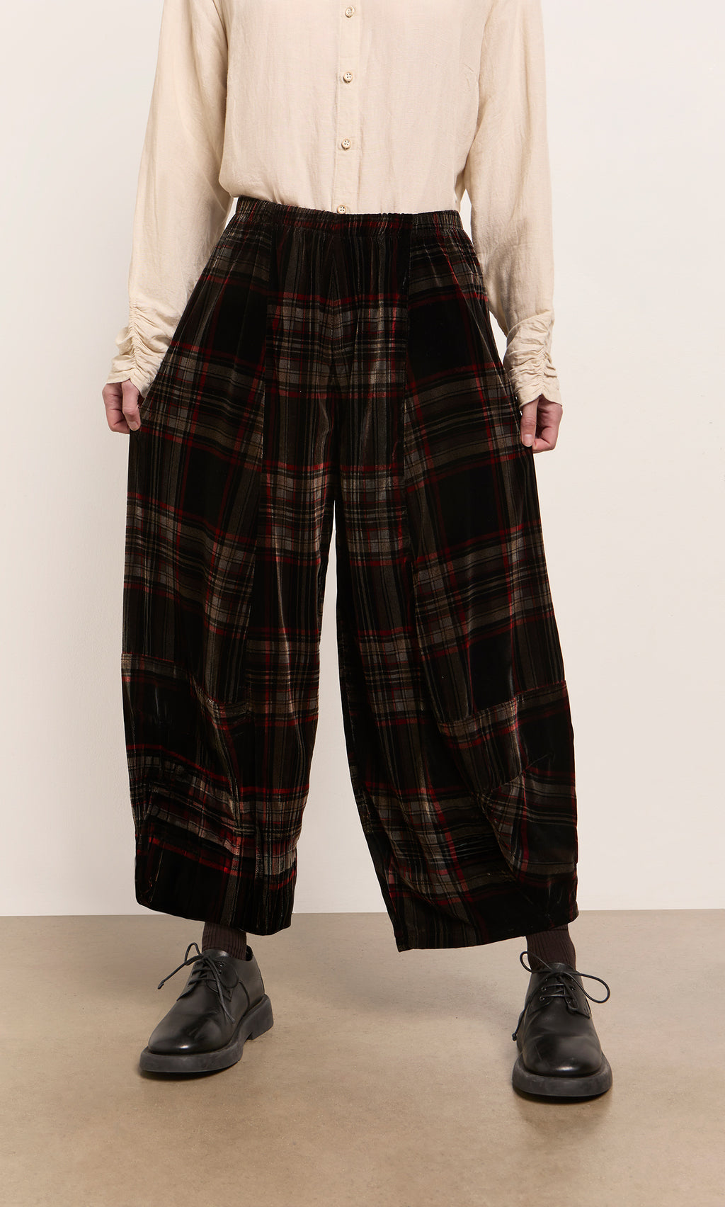 Plümo  Person wearing a cream shirt, Carson Tartan Pants, and black shoes stands against a plain background.