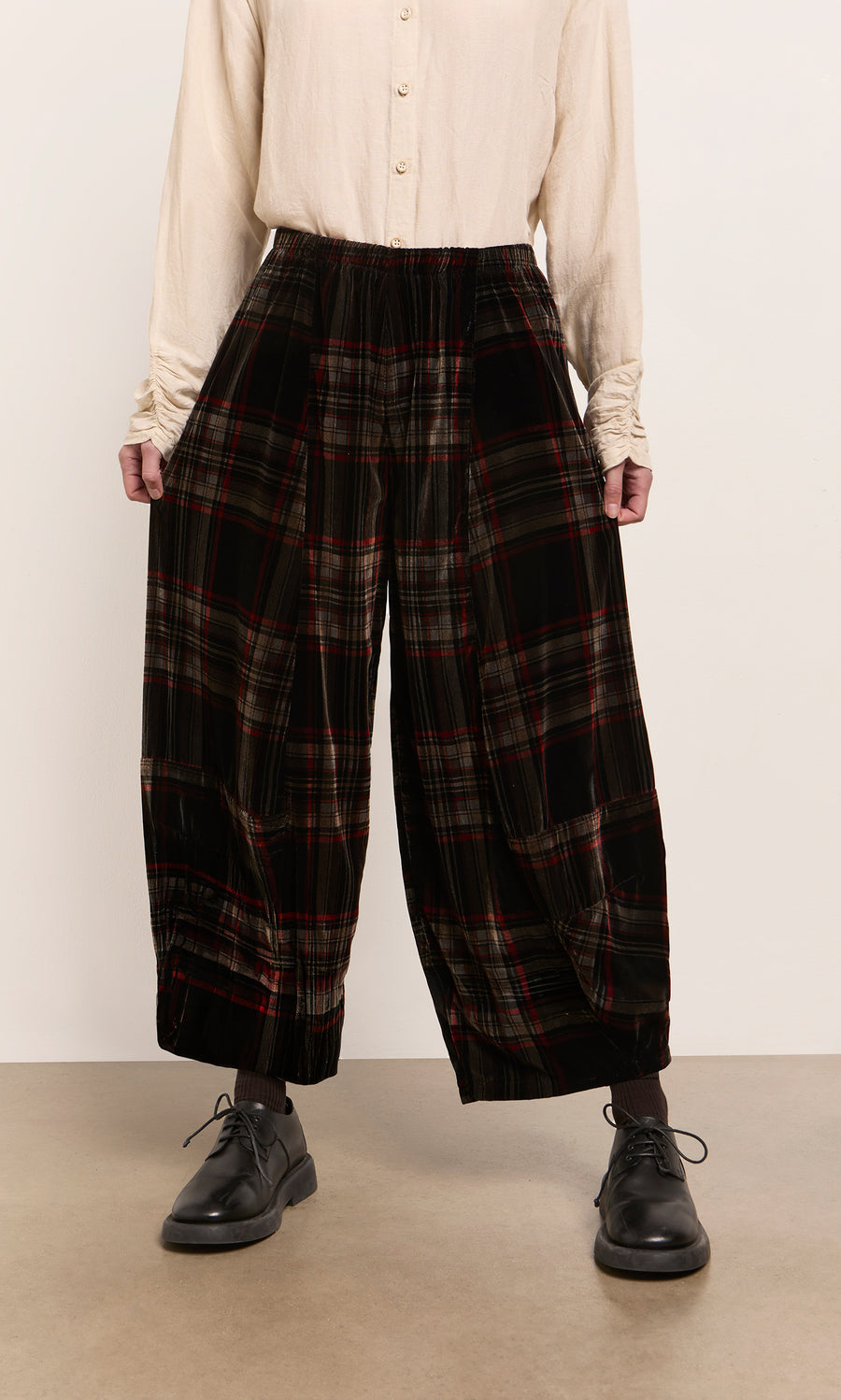 Plümo  Person wearing a cream shirt, Carson Tartan Pants, and black shoes stands against a plain background.