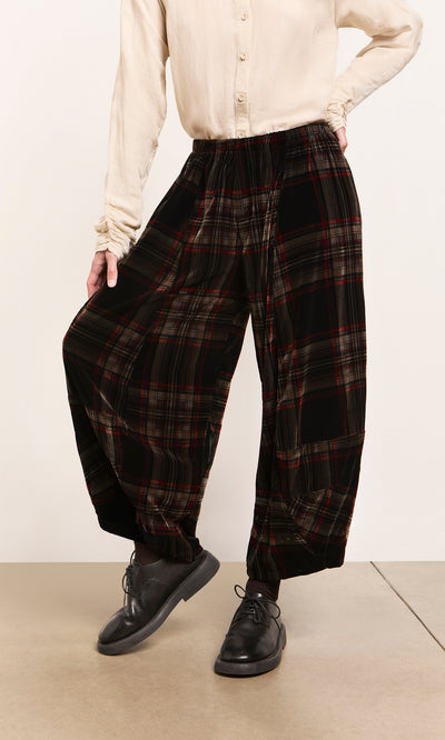 Plümo  Model in Carson Tartan Pants, cream blouse, and black shoes poses with hand on hip against beige backdrop.
