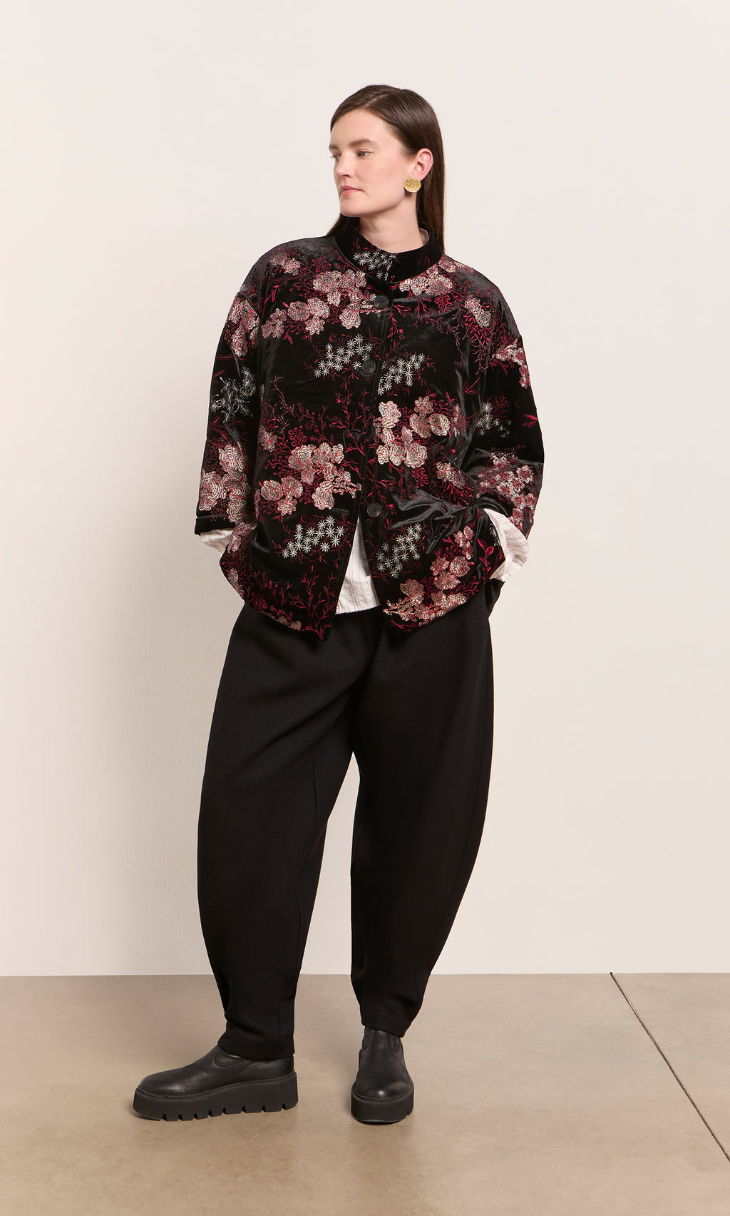 Plümo  Person in loose black pants, black boots, and the Charone Jacket stands against a plain light background.