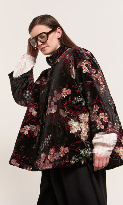 Plümo  Model in Charone Jacket in Chinoiserie velvet with chrysanthemums, white shirt, black pants, and oversized glasses.