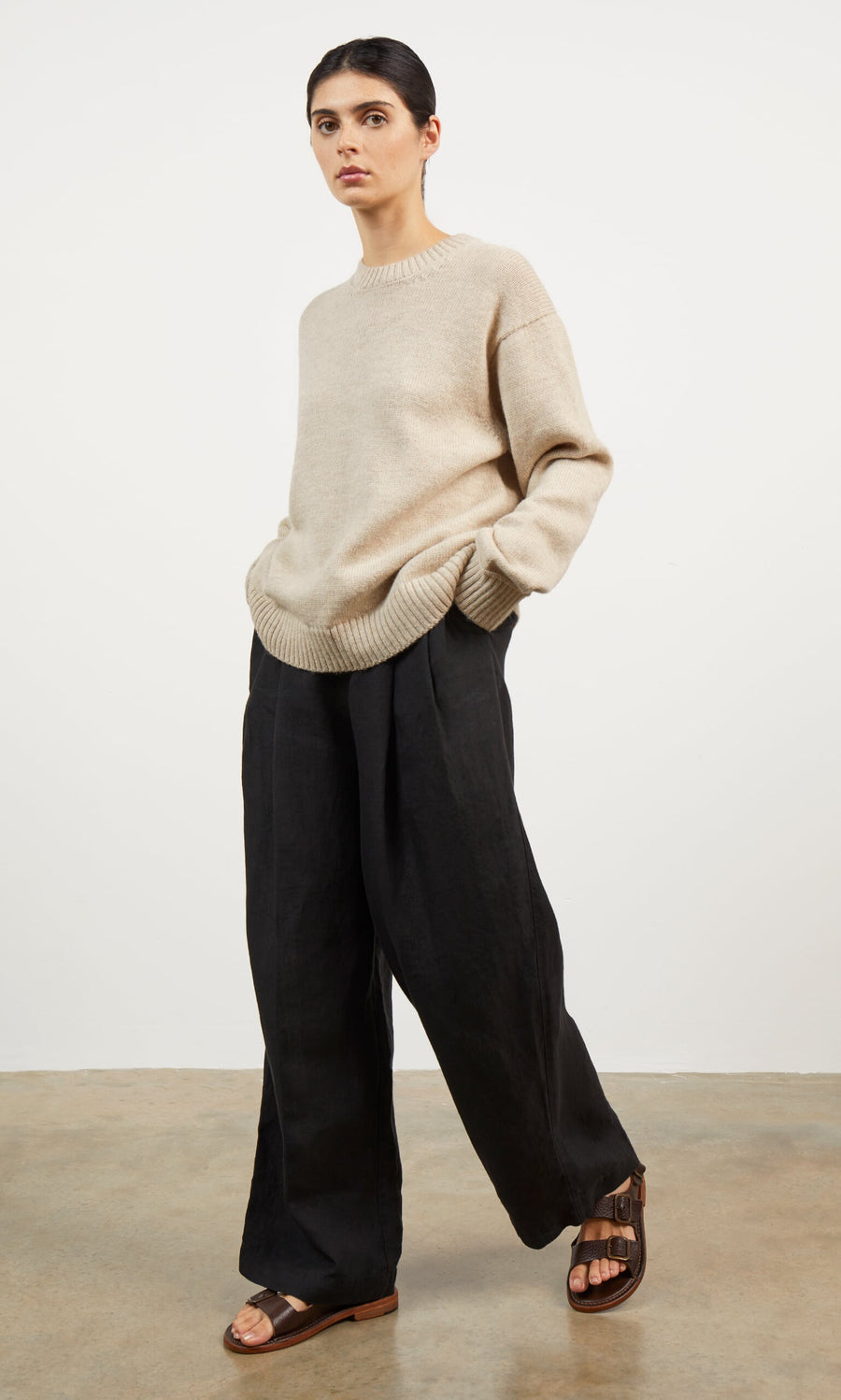 Plümo- A person in a Christie Wool Jumper, black wide-leg pants, and brown sandals stands with hands in pockets against a plain background.