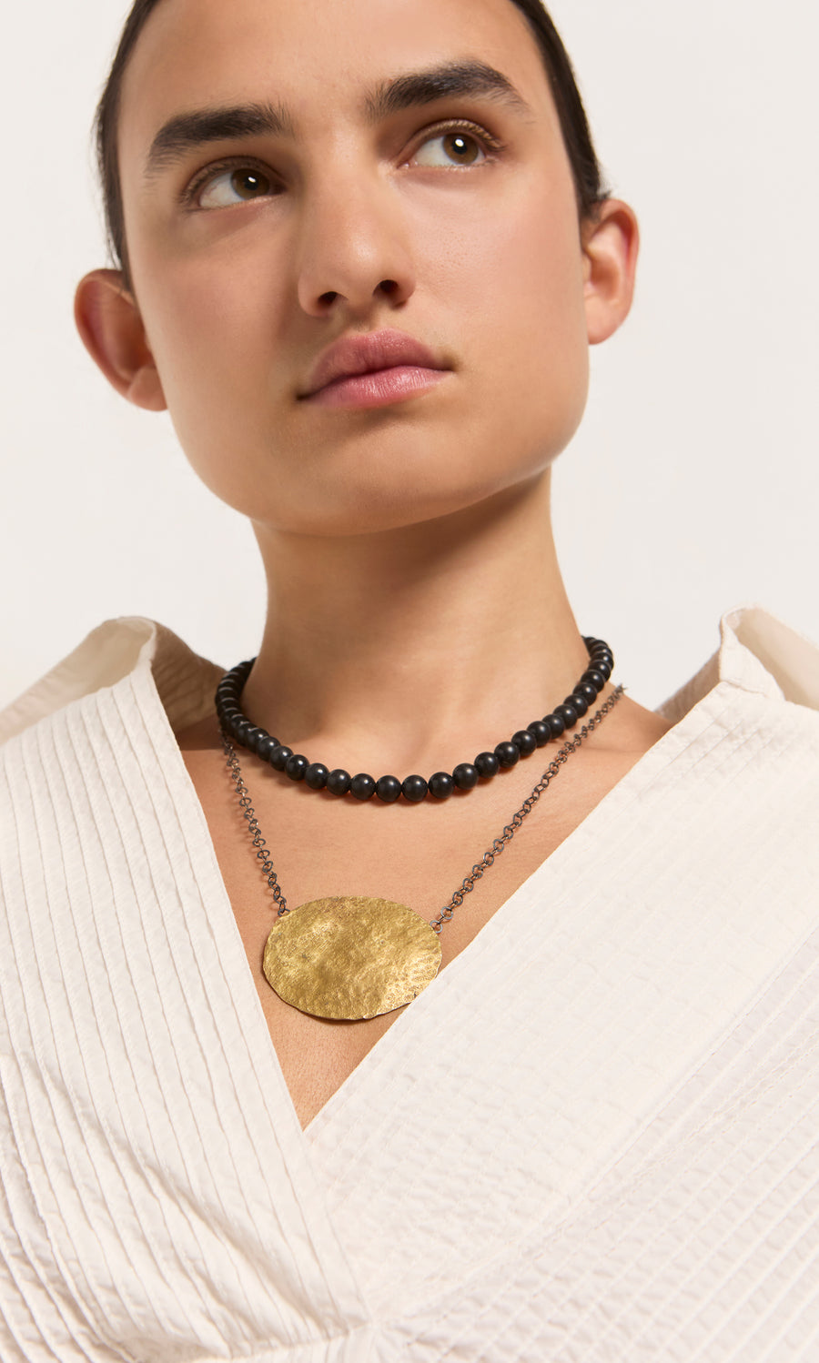 Plümo  Woman wearing a textured cream top, artisan black beaded necklace, and the statement gold Cressa Necklace.