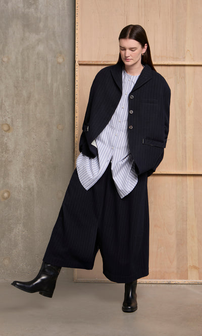 Plümo  Someone in the Bo Skirt, a striped shirt, and black boots stands by a wood and concrete background.