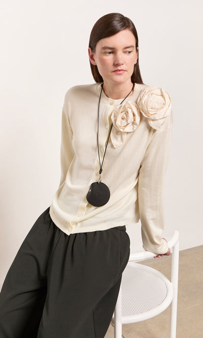 Plümo  Woman in cream cardigan with fabric roses holds a Coin Purse on String while sitting on a white chair.