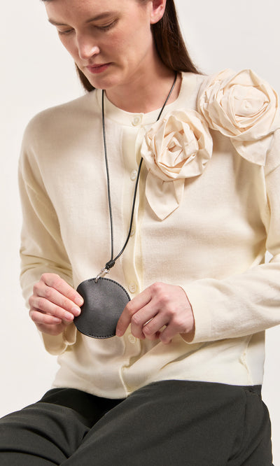 Plümo  Woman in cream cardigan holding the Coin Purse on String, a black Italian leather coin purse with a long cord.