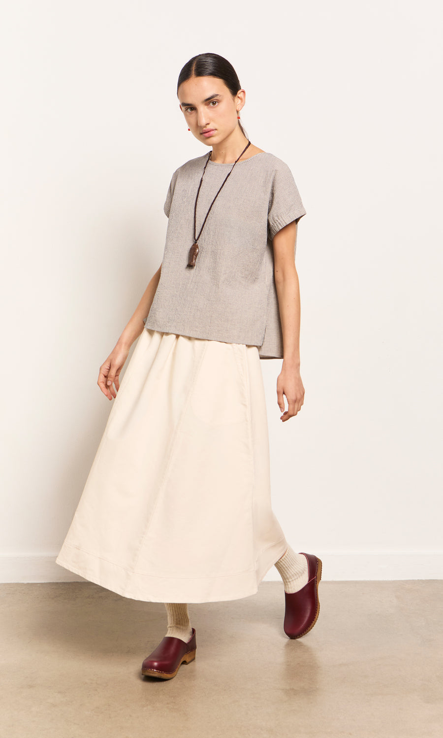 Plümo  Person in gray top, cream maxi skirt, red clogs, and Yumi Fish Necklace stands against a plain background.