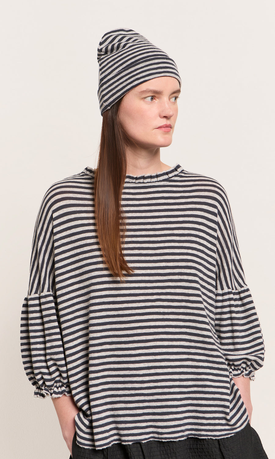 Plümo  Woman wearing the Dawn Stripe Beanie and loose puff-sleeve top, looking to the side.
