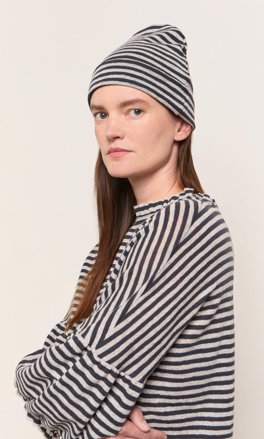 Plümo  Woman in a striped shirt and Dawn Stripe Beanie looks at camera against a plain light background.