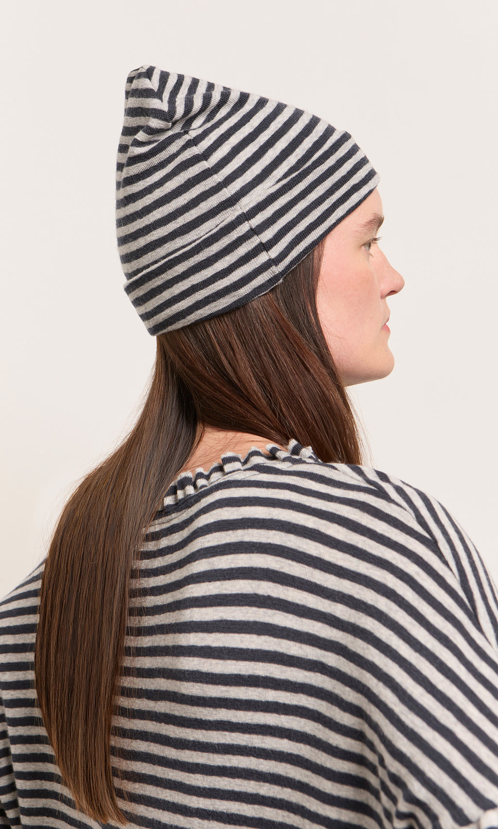 Plümo  Woman in profile wearing the Dawn Stripe Beanie, with her long brown hair showing from the back.