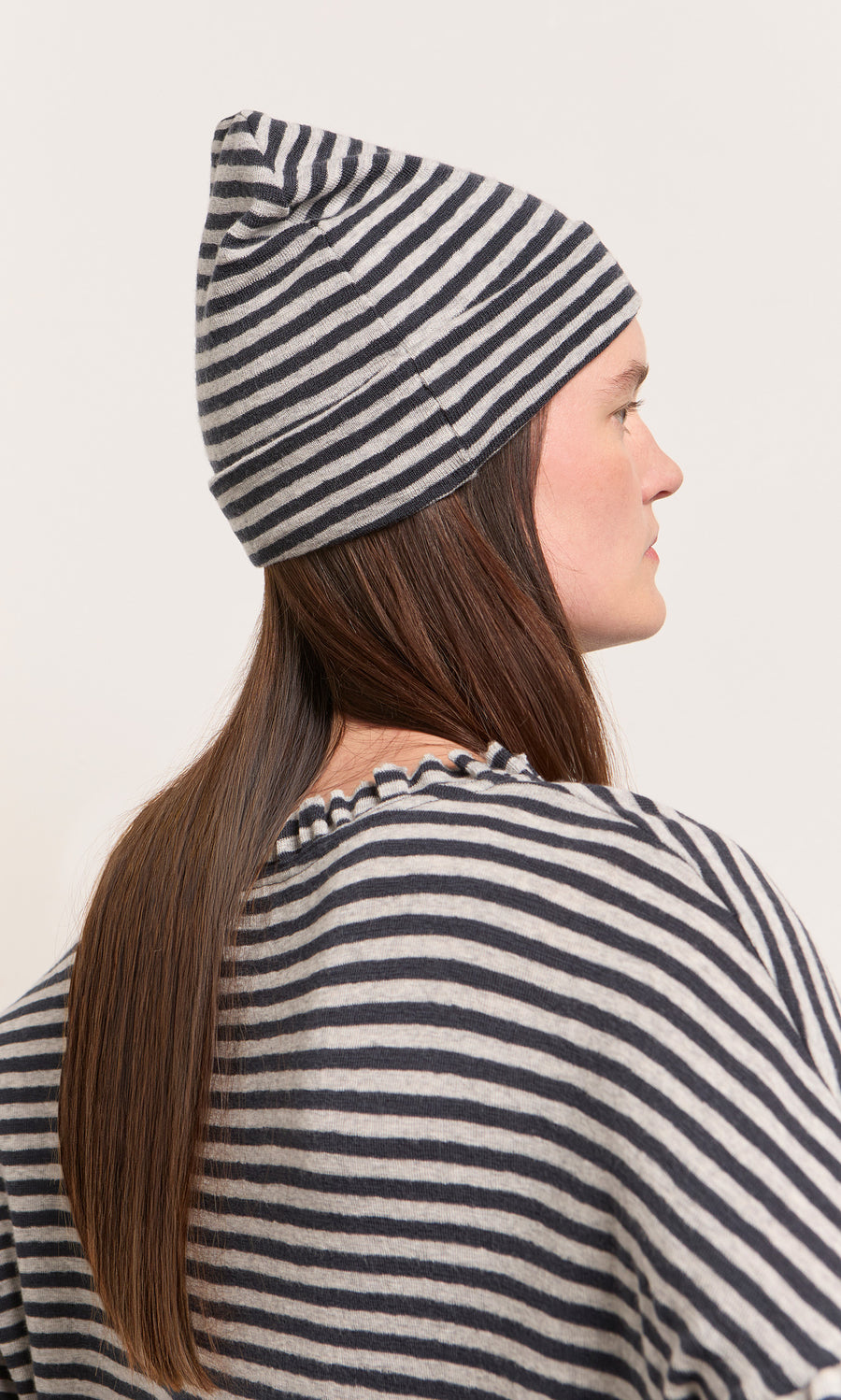 Plümo  Woman in profile wearing the Dawn Stripe Beanie, with her long brown hair showing from the back.