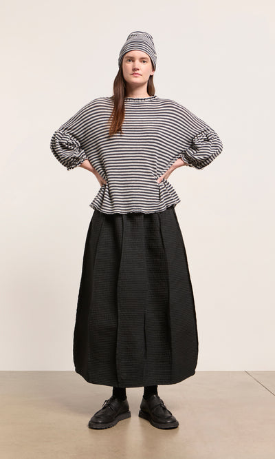 Plümo  Woman in Ruffle Top - Dawn Grey, striped shirt, hat, black skirt and shoes stands with hands on hips.