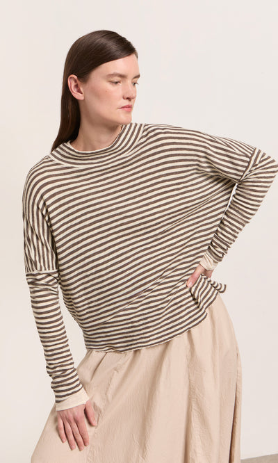 Plümo  Person wears the Oana Mock Neck sweater and a beige skirt, posing stylishly with one hand on hip.