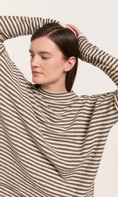 Plümo  Woman in the Oana Mock Neck sweater, arms raised, looking aside against a plain light background.