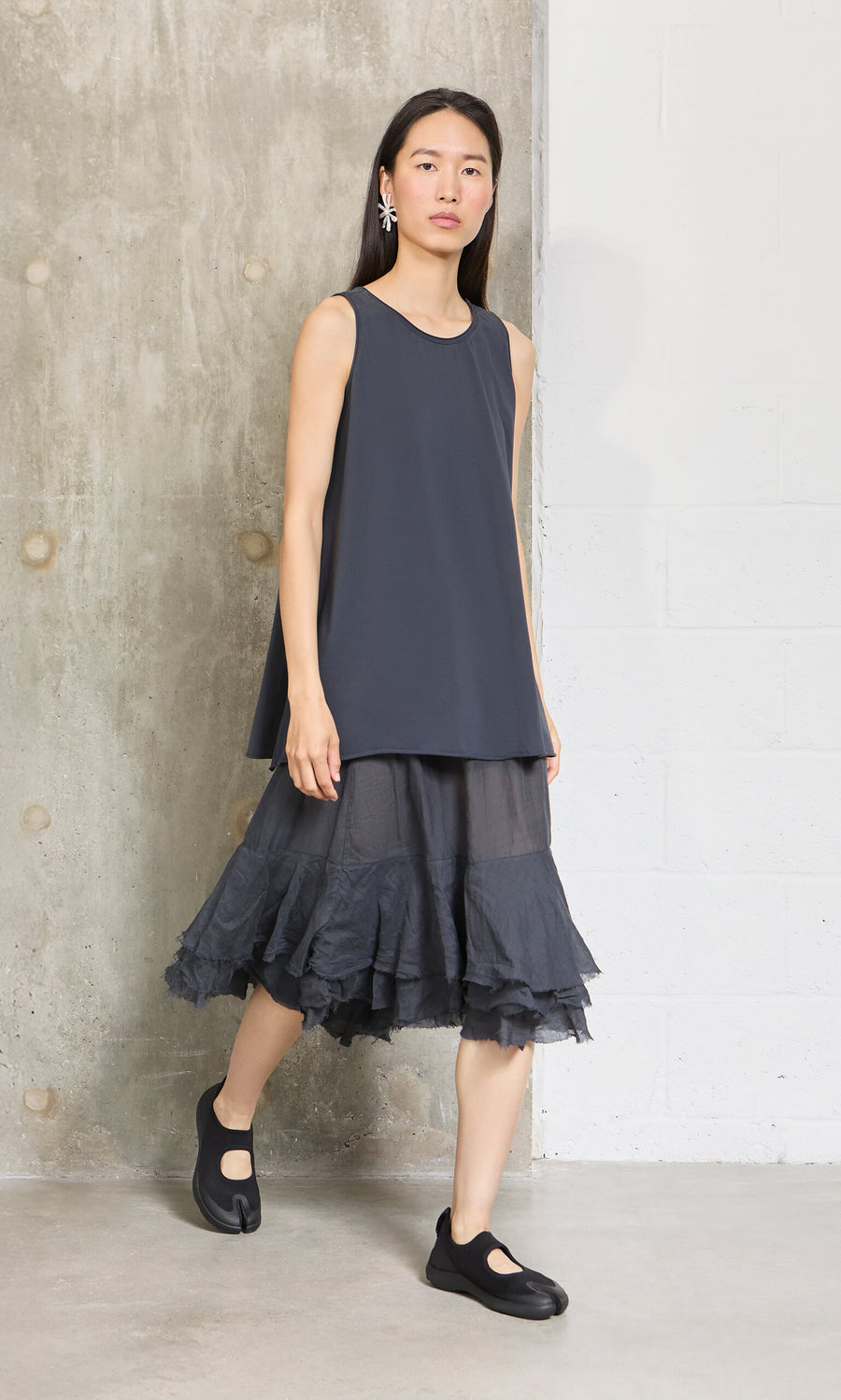 Plümo- Woman in the Edel Top and A-line black tulle skirt stands by a concrete wall in relaxed fit attire.