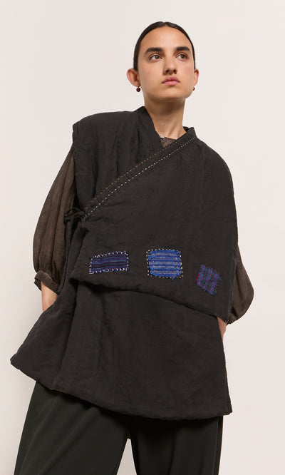 Plümo  Person wears the Engi Waistcoat layered over black, handstitched patches, posed against a plain light background.