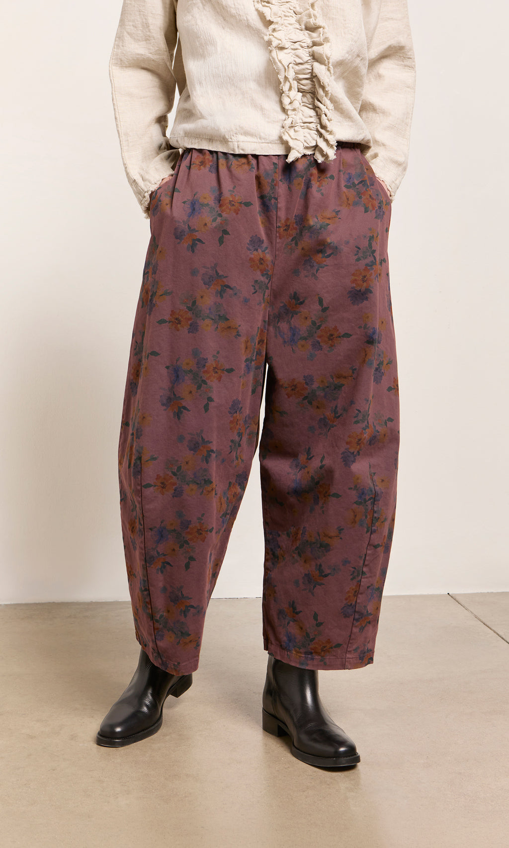 Plümo  Person in Espel Pants, a cream ruffled shirt, black ankle boots; hands casually in pockets.
