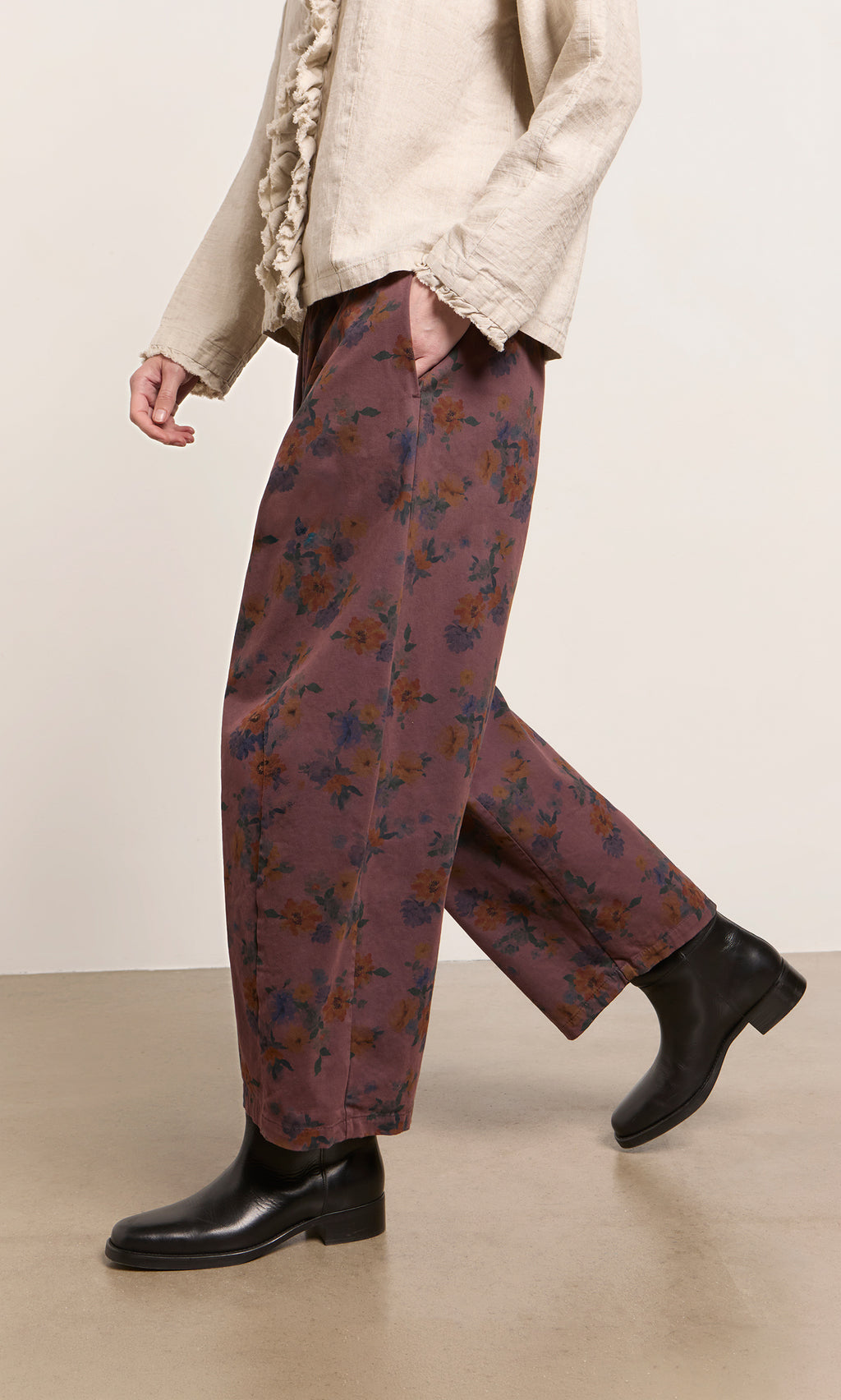 Plümo  Person in Espel Pants, black boots, and a beige textured long-sleeve top, walking indoors.