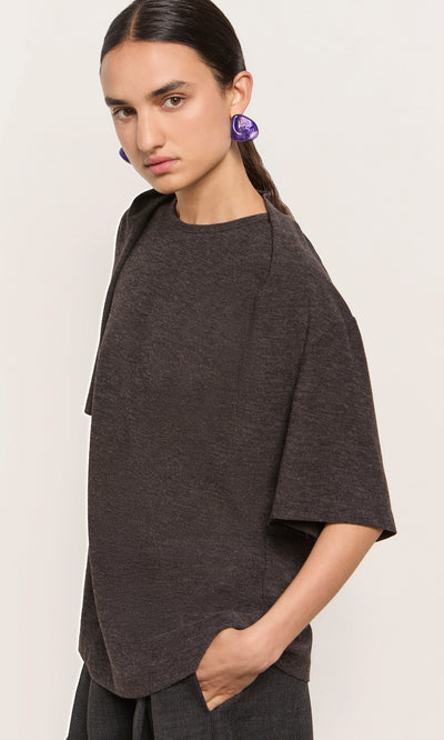 Plümo  Woman wearing the Feld Tee, hand in pocket, purple earrings, facing the camera.