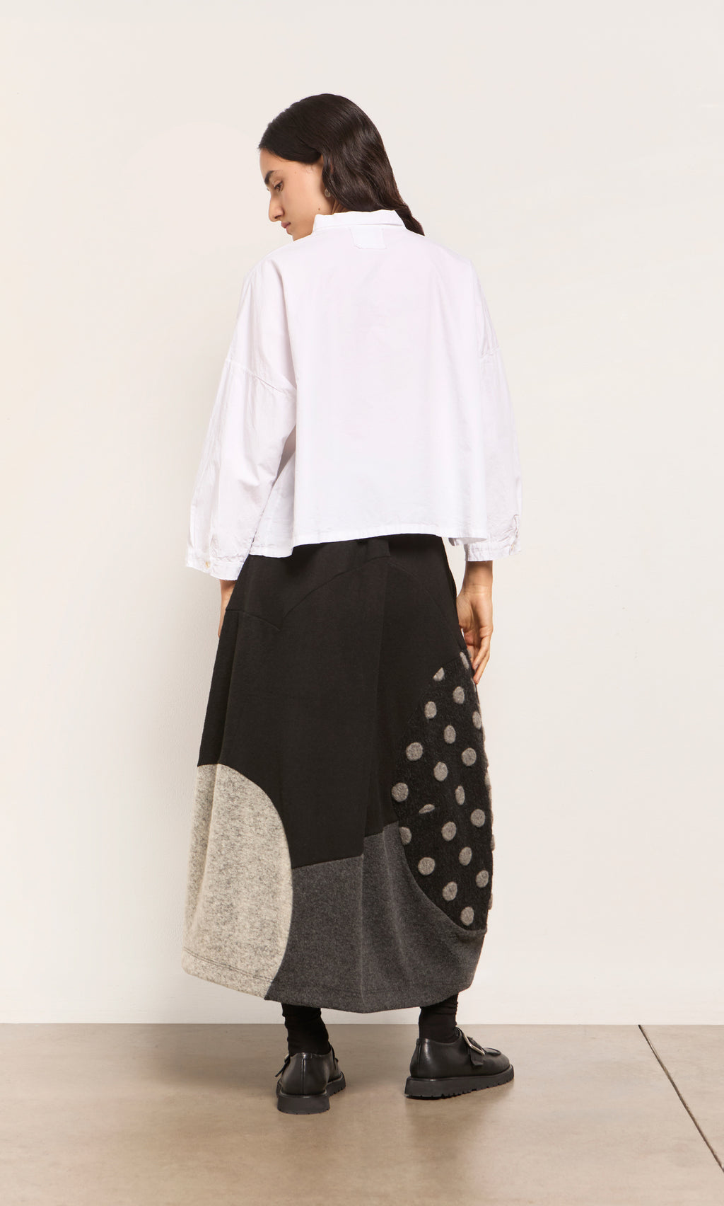 Plümo  Woman facing away in a white shirt and the Felted Bubble Skirt, a patchwork midi with geometric, polka dot patterns.