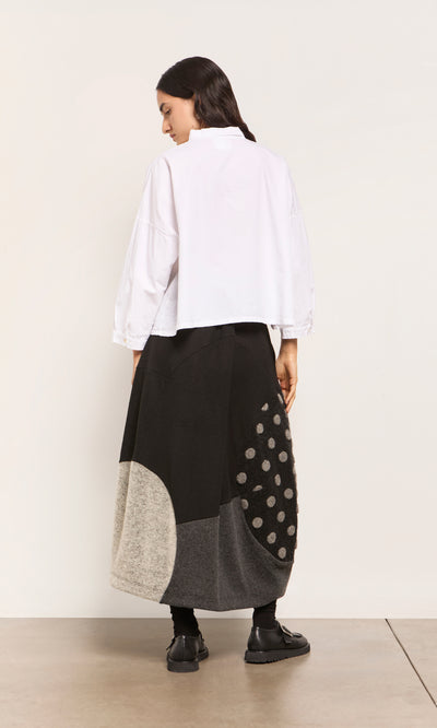 Plümo  Woman facing away in a white shirt and the Felted Bubble Skirt, a patchwork midi with geometric, polka dot patterns.