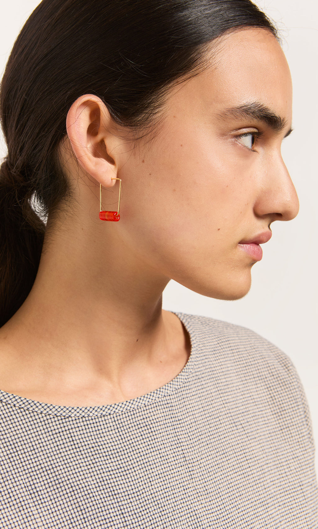 Plümo- Person with dark hair in a low ponytail wears Fortuna Earrings - Satsuma, shown in profile against a plain background.