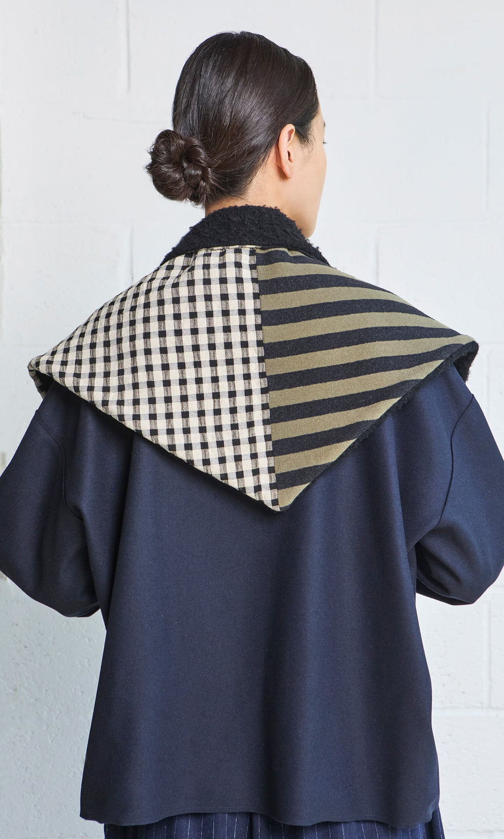 Plümo- Person with dark hair in a bun wearing the Porter Wool Top with a bold black and olive green checkered collar.