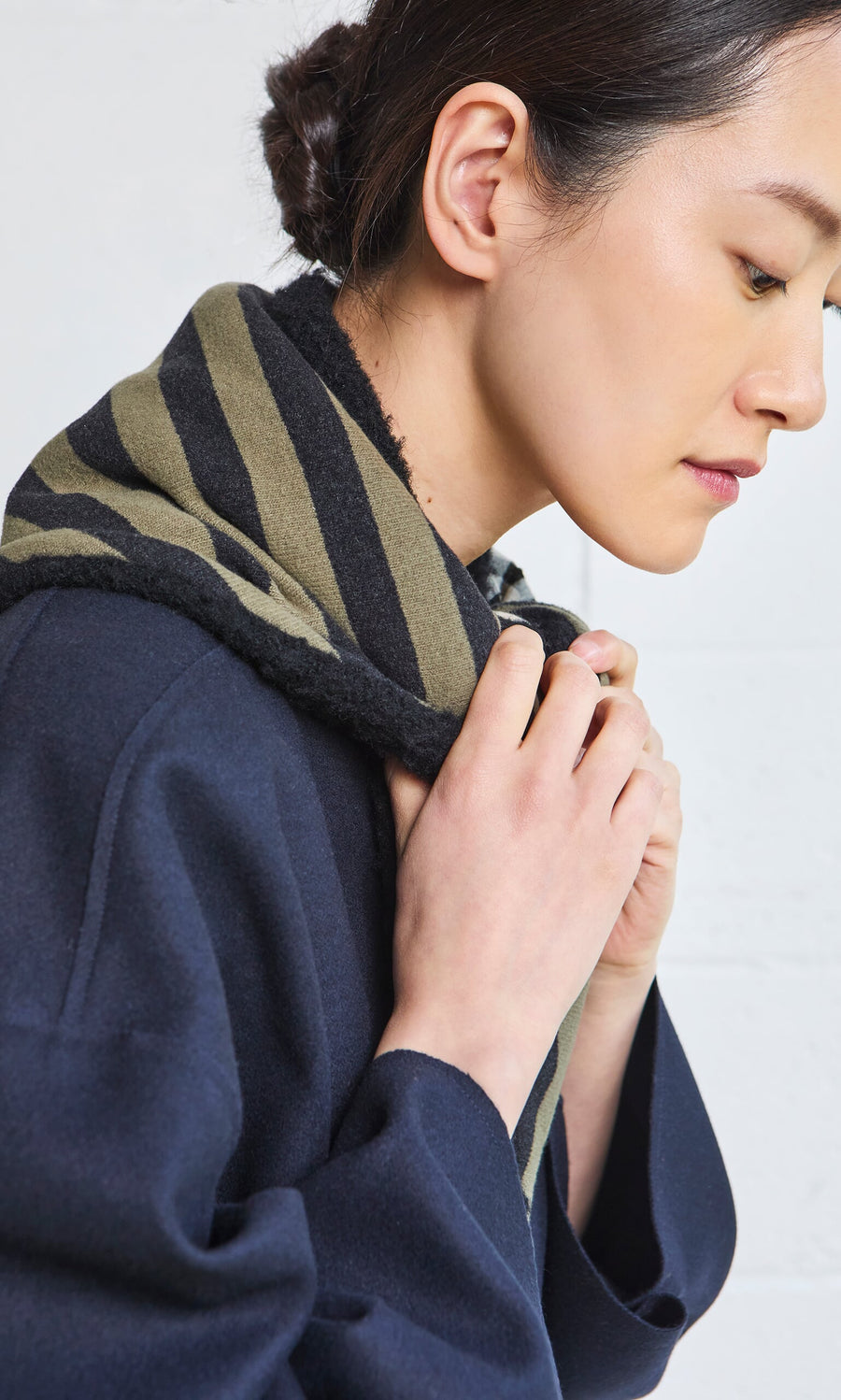 Plümo- Woman in profile wearing a navy coat and the Gingham Patch Scarf, looking down with hands near her neck.