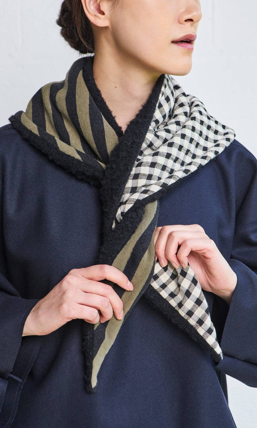 Plümo- Woman wearing a navy coat and adjusting the Gingham Patch Scarf with black stripes and checks.