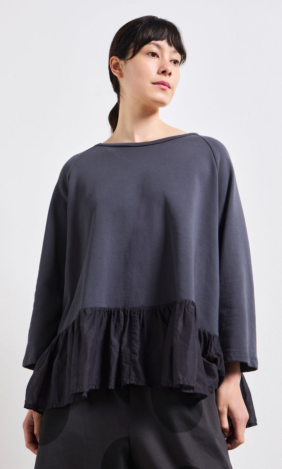Plümo- Woman wearing a Grey Ruffle Top, standing against a plain light background.