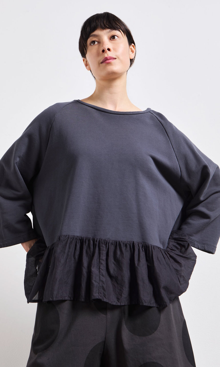 Plümo- Woman in a Grey Ruffle Top with peplum ruffles and wide sleeves, paired with black polka dot pants.