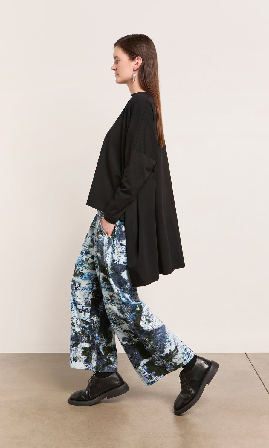 Plümo  Woman in a loose black top and Caccia Pants with a wintry print walks with hands in pockets.