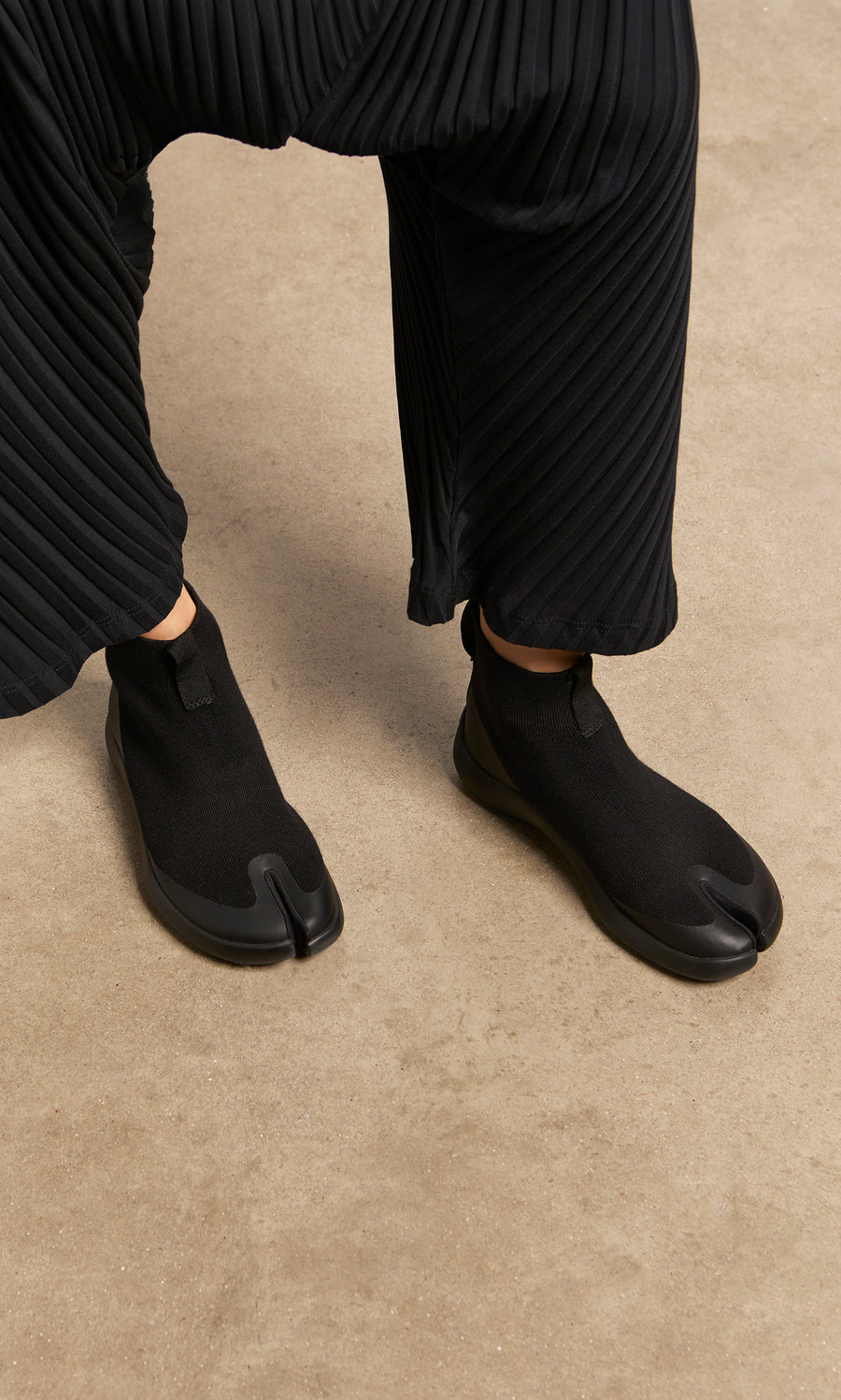 Plümo  Person wearing Higher Tabi Boots and pleated black pants, standing on a tan floor.