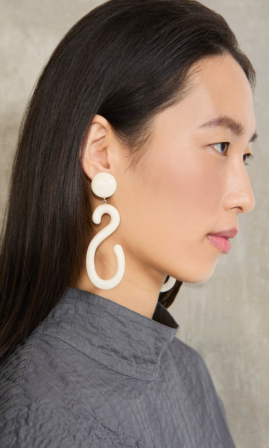 Plümo- Woman in gray top models large Horn Clip-On Earrings, facing left against a neutral background.