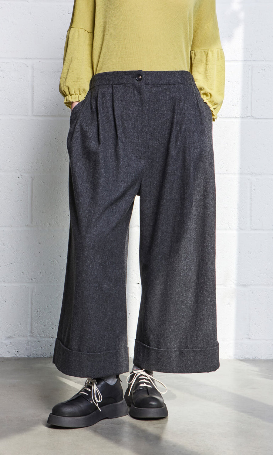 Plümo- Person wearing Horton Pants, black shoes, and a yellow long-sleeve top, standing indoors.