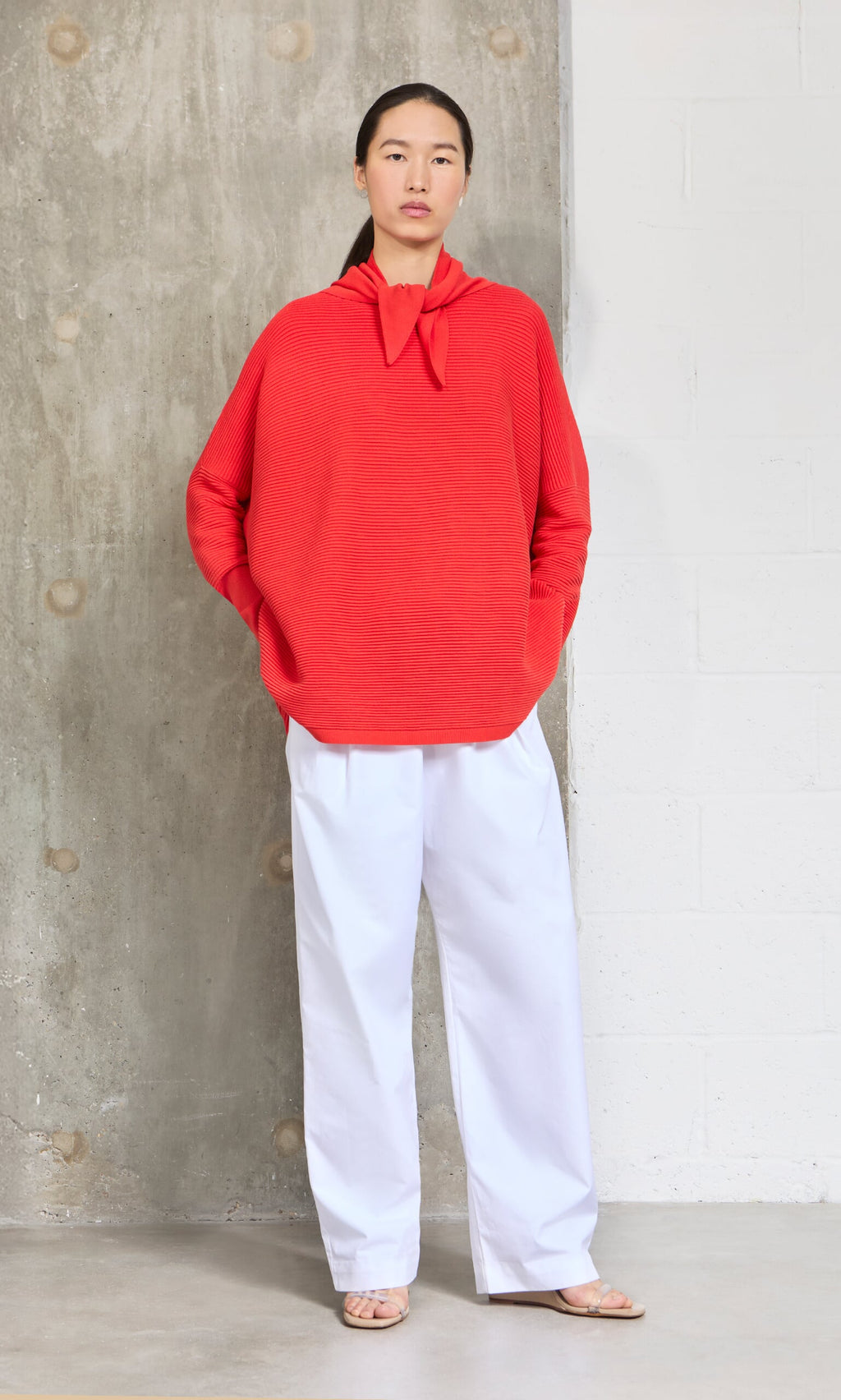 Plümo- A person stands against a concrete wall wearing the Jona Necktie - Lava, white wide-leg pants, and sandals.