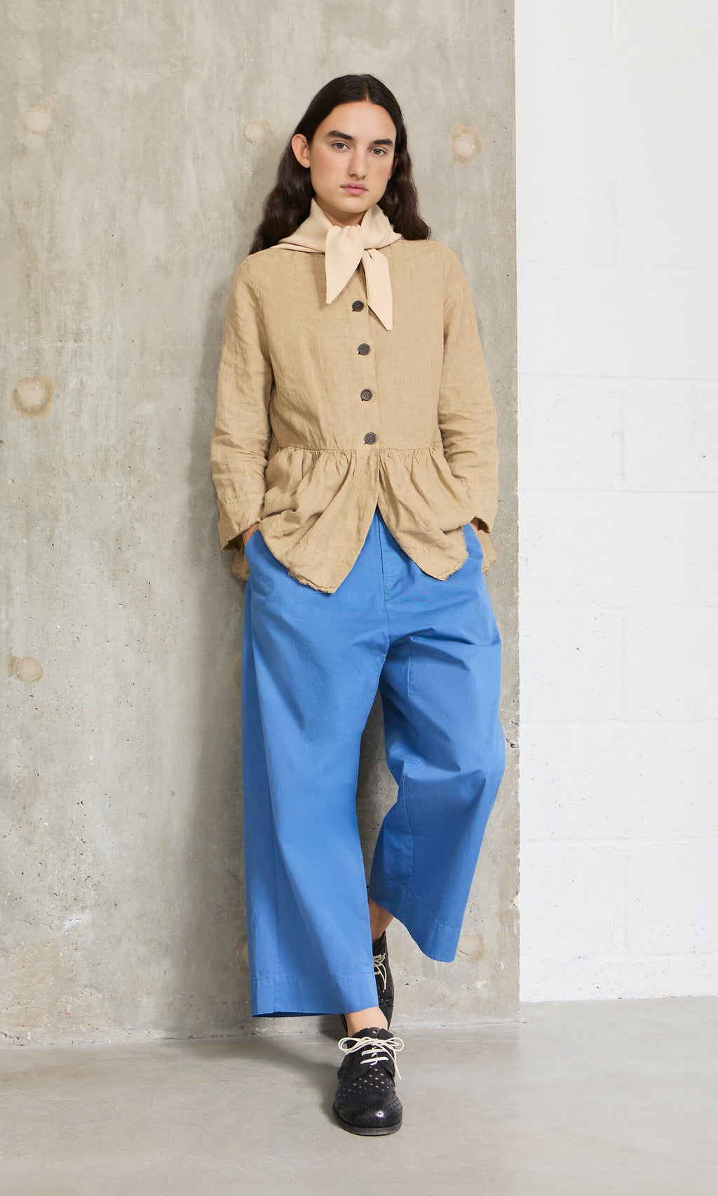 Plümo- Person wears the Jona Necktie - Silt, styled with a tan buttoned top and wide blue pants, posing by a concrete wall.