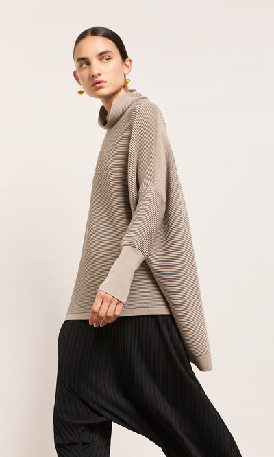 Plümo  Person in the Jack Rollneck – Miso and black pleated pants, standing against a plain light background.