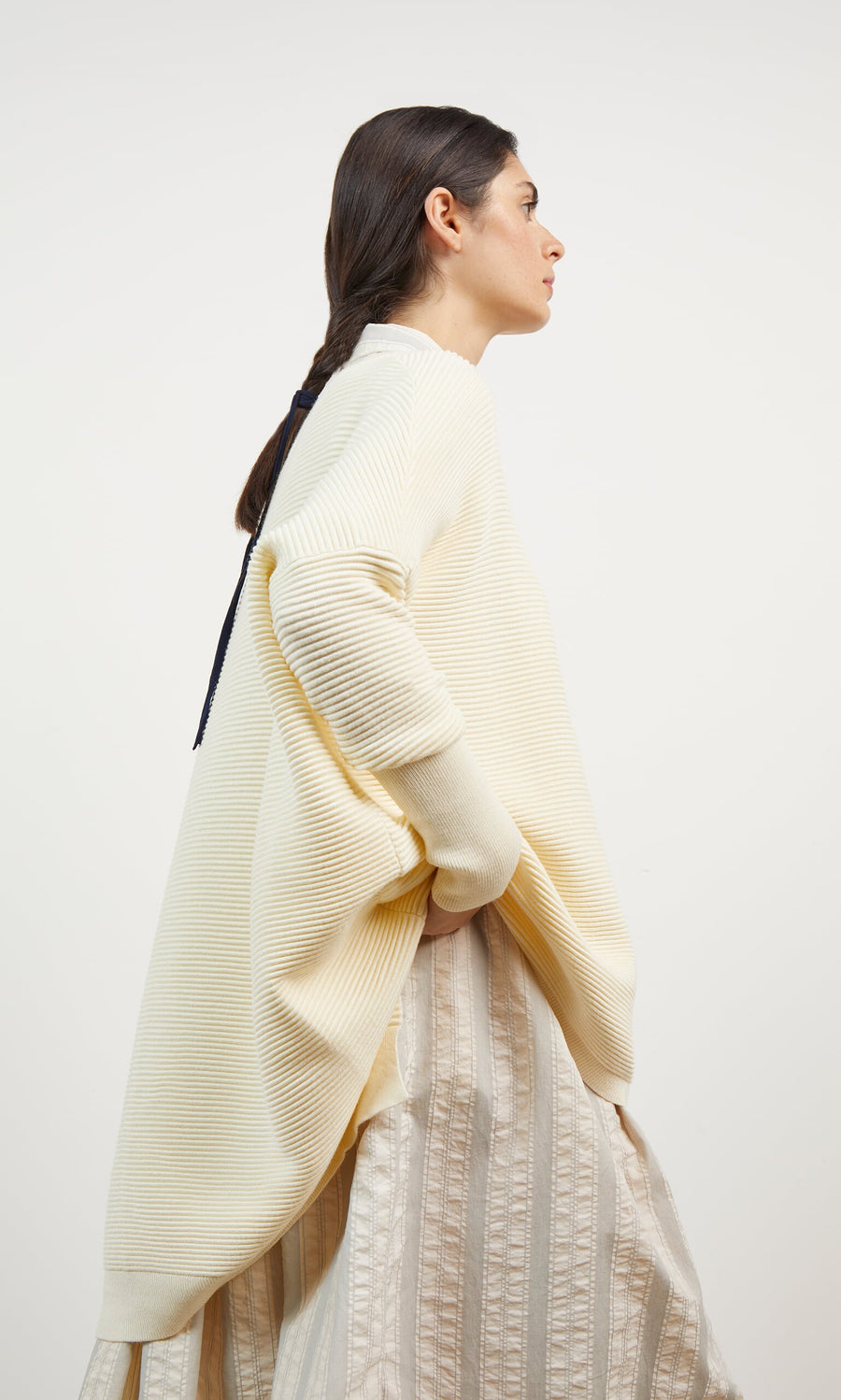 Plümo- Woman wearing the Jack Sweater - Cloud, an oversized cream ribbed style with dropped shoulders, stands sideways.