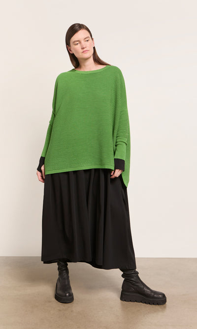 Plümo  Person wears a Jack Sweater - Pickle Green, long black skirt, and black boots against a plain background.