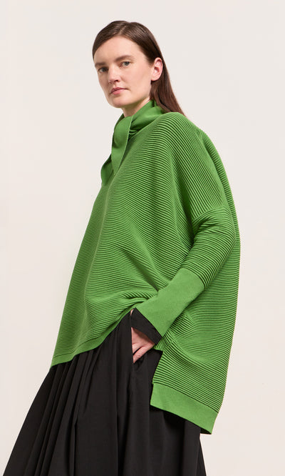 Plümo  Person wearing a Jack Sweater - Pickle Green and black skirt, standing against a plain light background.