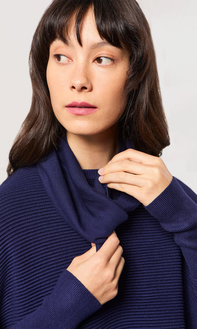 Plümo- Woman with long dark hair wearing a navy Jona Necktie, holding the collar and looking to her left.