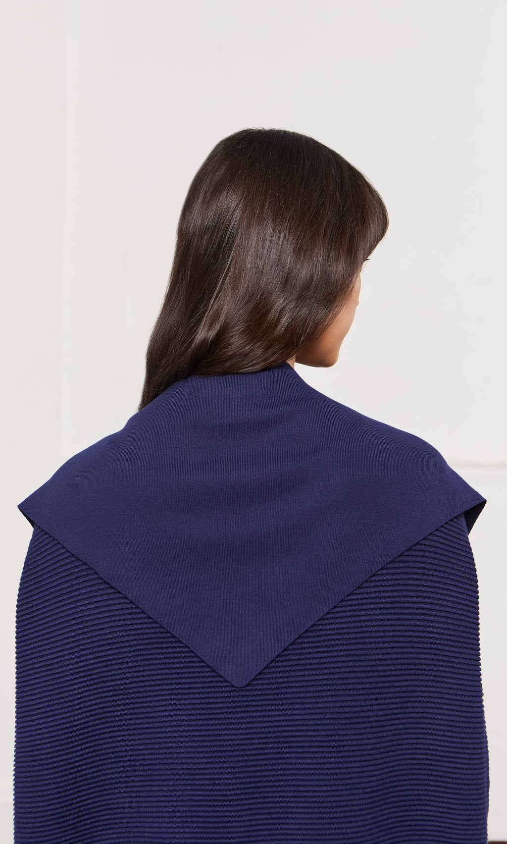 Plümo- A person with long dark hair wears a navy Jona Necktie featuring a distinctive triangular collar.