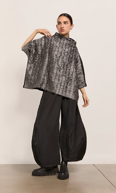 Plümo  Person in a loose gray top and black Hooley Pants stands against a plain background.