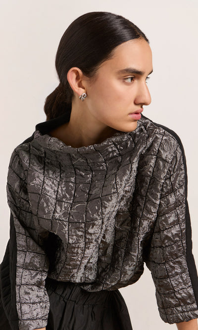 Plümo  Woman with dark hair in a low ponytail wears the oversized Jorn Top and silver earrings, looking to the side.