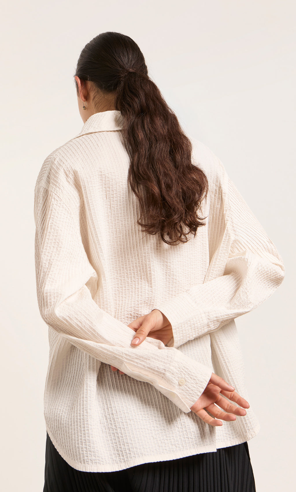Plümo  A person with long brown hair in a ponytail wears a textured Kaburi Shirt, hands behind their back.